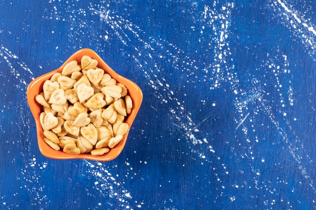 Pile of salted heart-shaped crackers placed in orange bowl. 