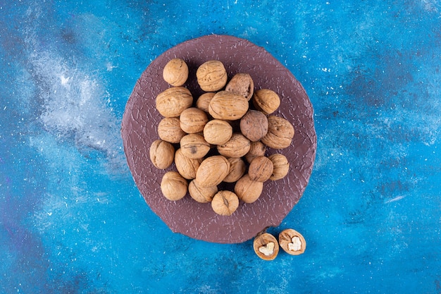 Pile of shelled walnuts on wood piece on blue table.