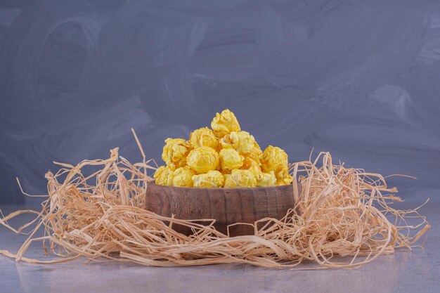 Куча соломы под небольшой деревянной миской, наполненной конфетами из попкорна на мраморном фоне. Фото высокого качества