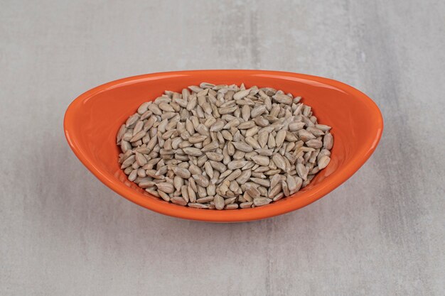 Pile of sunflower seeds in orange bowl.