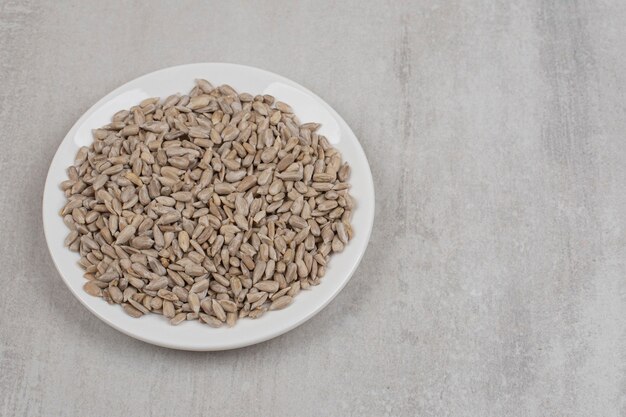 Pile of sunflower seeds on white plate.