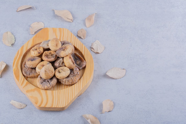 Pile of sweet dried figs placed on wooden plate with leaves. 