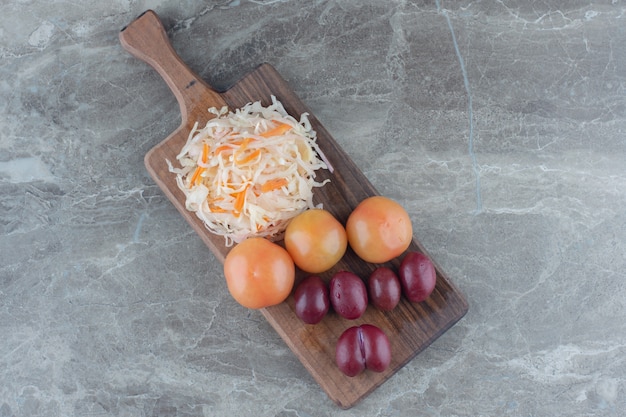 Pile of tasty fermented cabbage with vegetables on wooden cutting board.