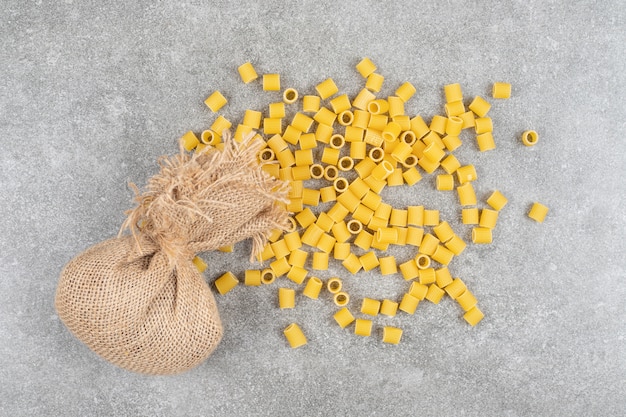 Pile of uncooked pasta and sackcloth on marble surface