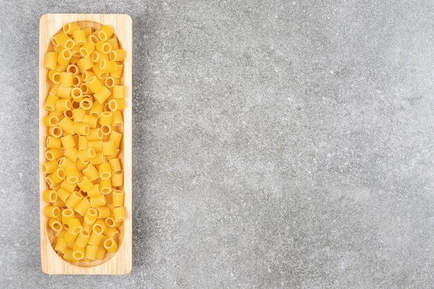 Pile of uncooked pasta on wooden plate 