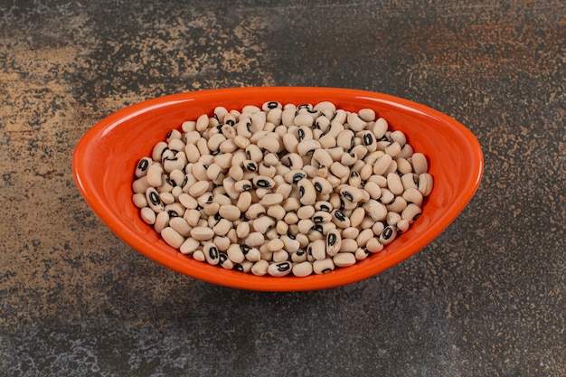 Pile of uncooked white beans in orange bowl. 