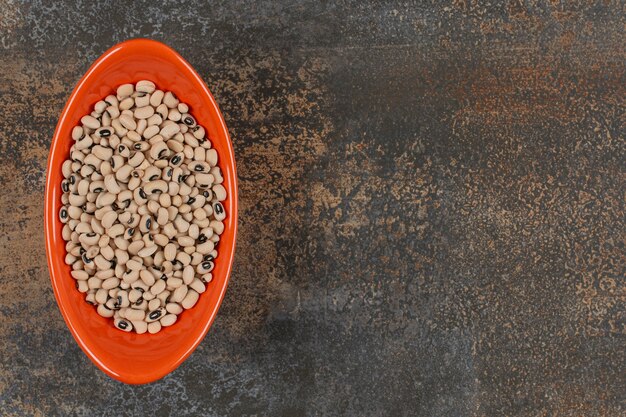 Pile of uncooked white beans in orange bowl. 