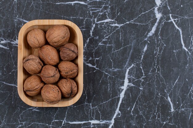 Pile of walnut in wooden bowl over black.