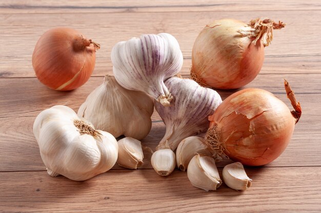 Pile of whole onions and garlic bulbs and cloves on a wooden table