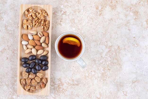 Piles of candy and various nuts in a small tray next to a tea mug 