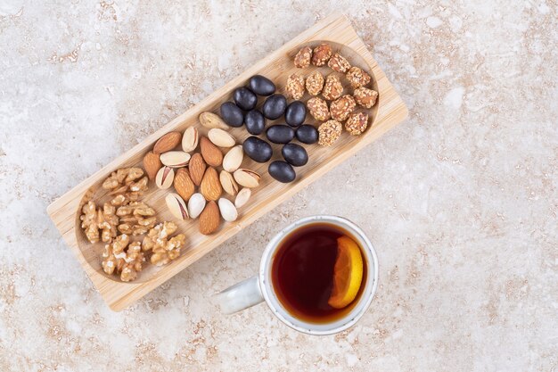 Piles of candy and various nuts in a small tray next to a tea mug 