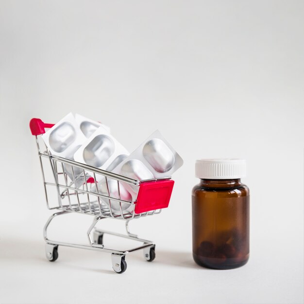 Pill blisters in shopping cart with glass bottle on white background