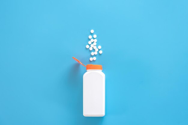 Pills are poured out of a jar on a blue background flat lay