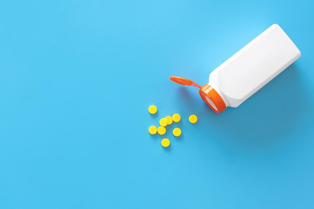 Pills are poured out of a jar on a blue background flat lay