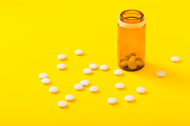 Pills bottle and circular white medicine on yellow background