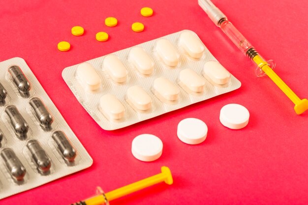 Pills, capsules and syringe on bright red background