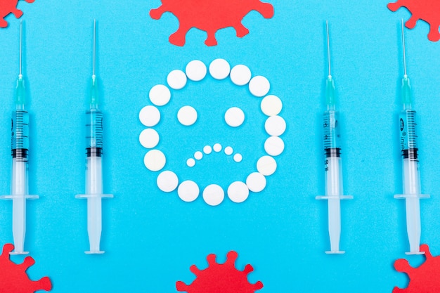 Pills forming sad emoji with needles around with virus