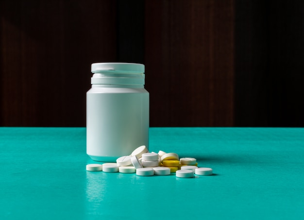 Pills and pill bottle on a cyan blue and black background. side view.