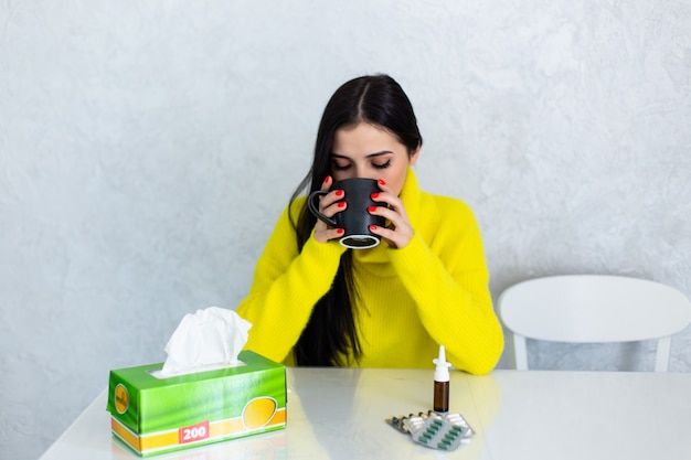 Pills and tea. Young woman taking pills and drinking hot tea having cold