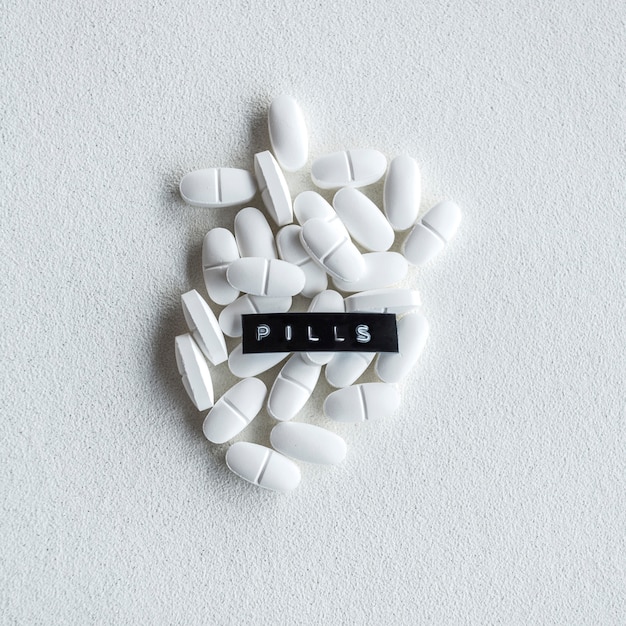 Pills text over the oval white tablets on rough background