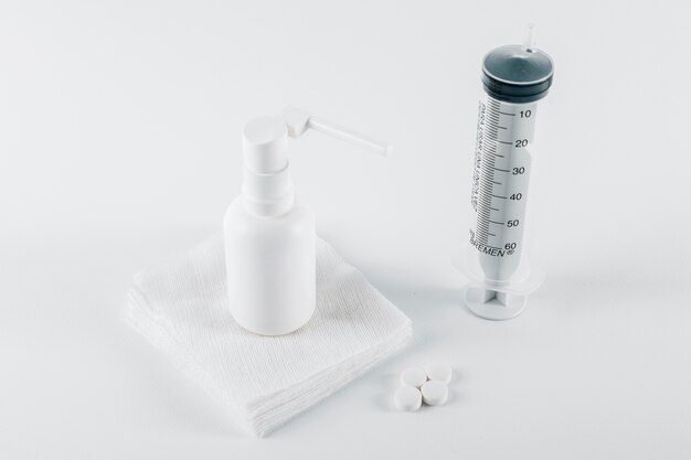 Таблетки; белый баллон спрей на медицинской марле и пустой шприц для лечения на белом фоне