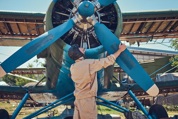 Pilot or mechanic in a full flight gear checks the propeller of his retro military aircraft before the flight.