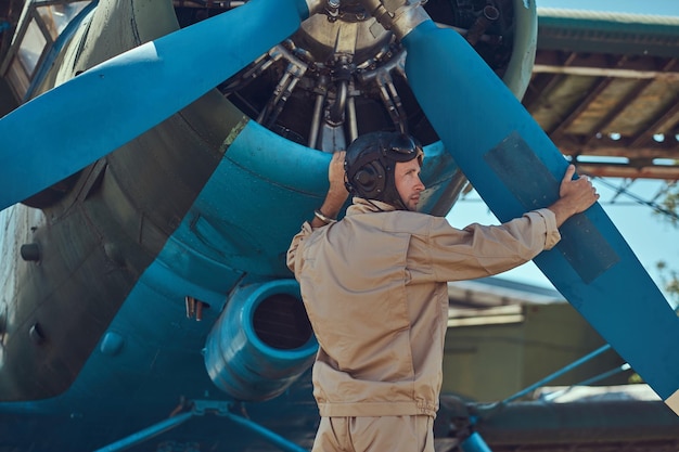 Pilot or mechanic in a full flight gear checks the propeller of his retro military aircraft before the flight.