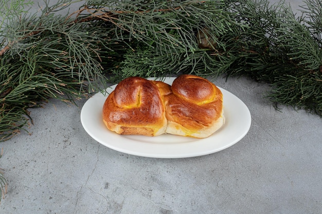 Free photo pine branches behind a platter of sweet bun on marble table.