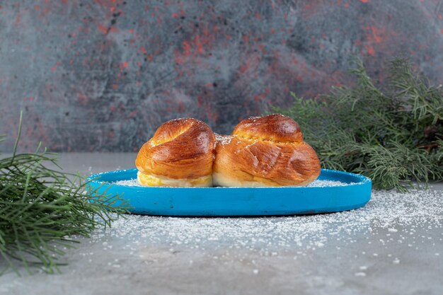 Pine branches next to a small platter with a sweet bun on marble table.