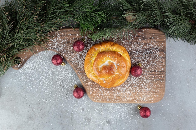 Free photo pine branches, wooden board, christmas tree toys and a small bun on marble surface