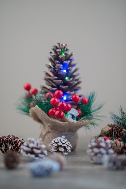 Pine cone decorated with holly berries and lights on wooden table.