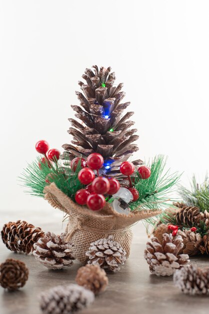 Pine cone decorated with holly berries and lights on wooden table.