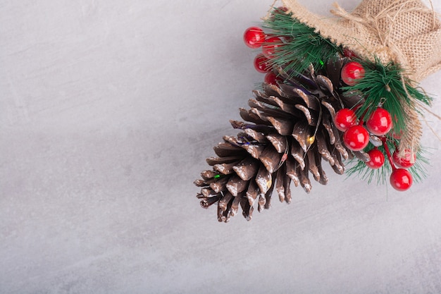 Pine cone decorated with holly berries and snowflake on white surface