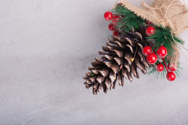 Pine cone decorated with holly berries and snowflake on white surface