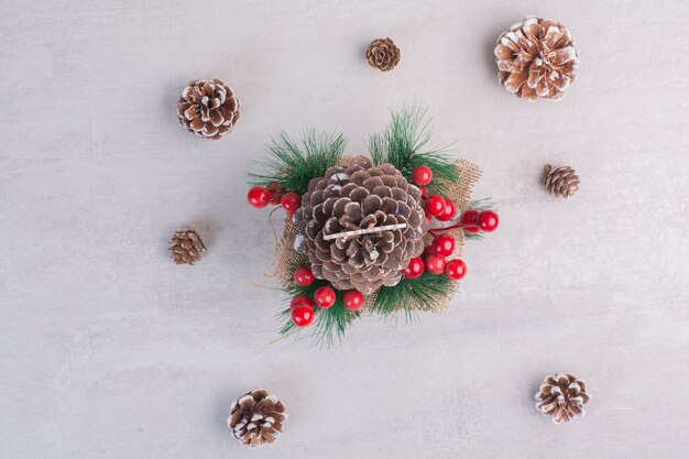 Pine cone decorated with holly berries and snowflake on white table