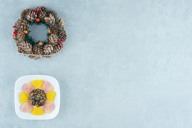 Pine cone wreath and a platter of marmelades and a donut on marble.