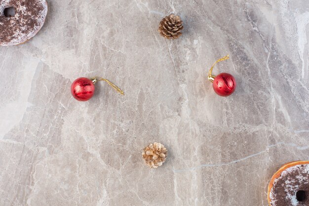 Сосновые шишки, рождественские украшения и пончики на мраморе.