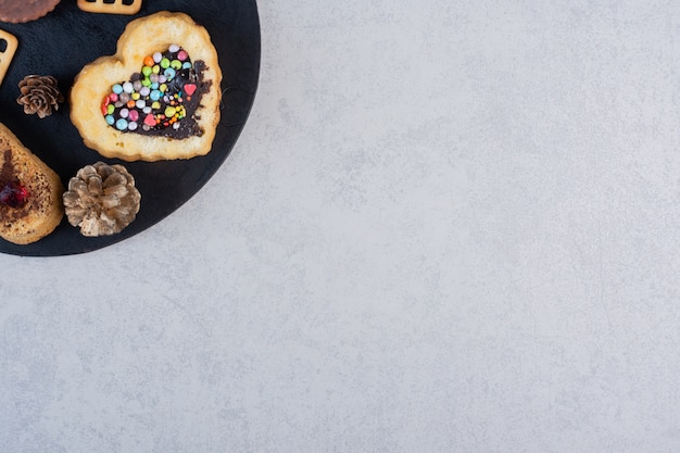 Pine cones, cookies, cakes and crackers on a black board on marble table.