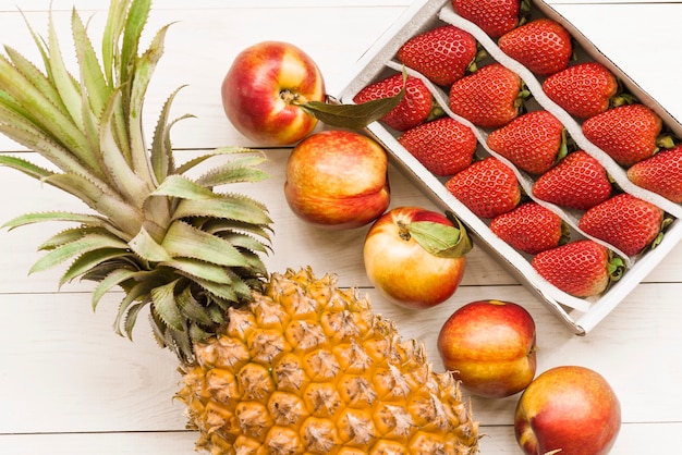 Foto gratuita ananas; mele e fragole sullo sfondo in legno