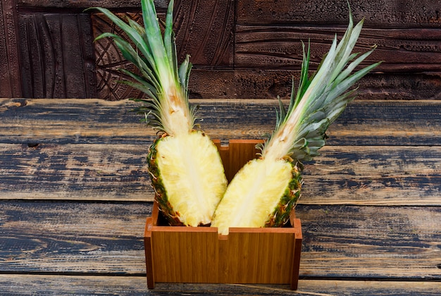 Pineapple cut in a half in a wood plate on old wood and dark stone tile, side view.