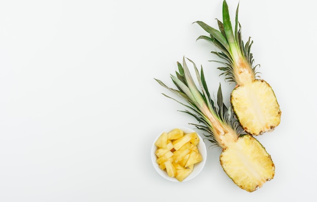 Pineapple cut in halves and slices in a white bowl on a white. flat lay.