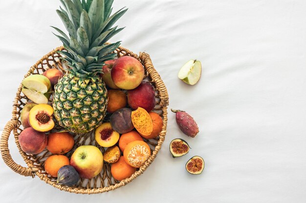 Pineapple and other exotic fruits in a basket on a white background top view