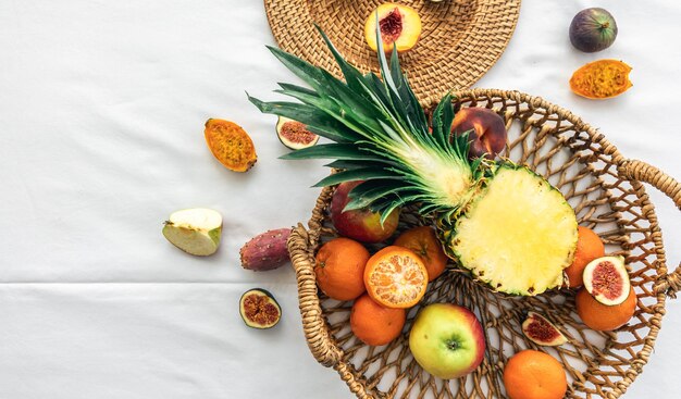 Pineapple and other exotic fruits in a basket on a white background top view