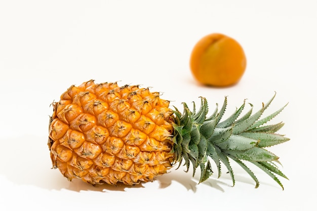 Pineapple behind a peach on a white