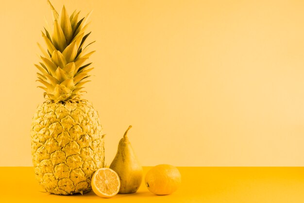 Pineapple; pear and halved lemon on yellow background