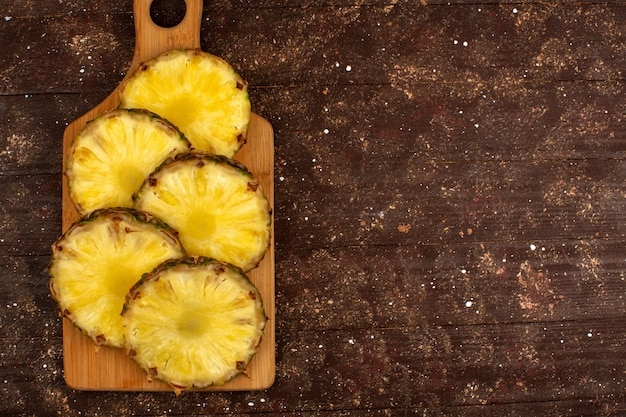 Foto gratuita i pezzi dell'ananas hanno affettato succoso maturo fresco una vista superiore sullo scrittorio di legno marrone e sul fondo rustico