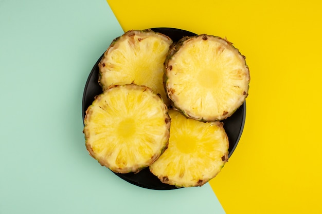 Pineapple rings fresh juicy mellow inside black plate a top view on a colorful desk