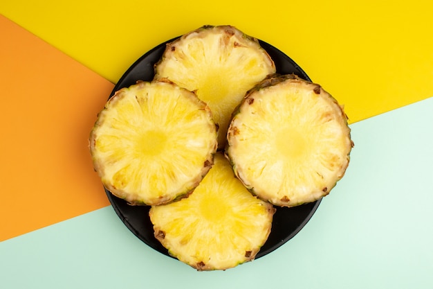 Pineapple slices fresh ripe mellow juicy rings inside black plate on a colorful floor