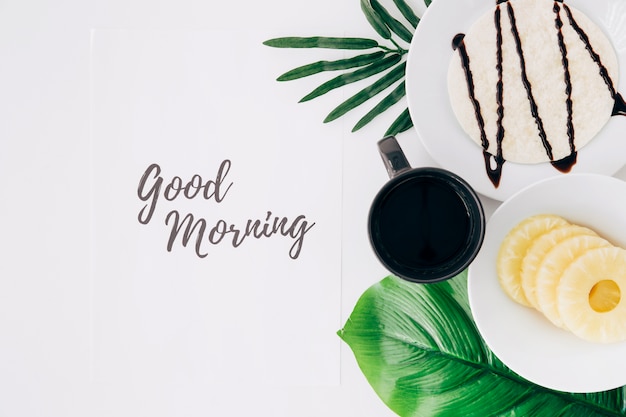 Pineapple slices; tortillas and coffee on leaves with good morning text on paper over white background