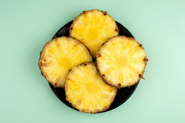 Pineapple a top view of sliced ripe mellow fresh inside black plate and on a blue